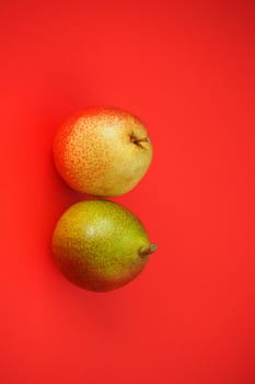 Ripe fruit on a red background. Beautiful pears and apples, Vertical image. Close-up.