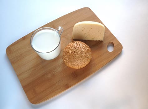 A piece of cheese with baguette and a glass of milk on a wooden tray.