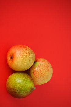 Ripe fruit on a red background. Beautiful pears and apples, Vertical image. Close-up.