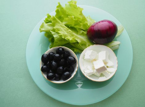Ingredients for Greek salad feta cheese and black olives in a salad bowl.