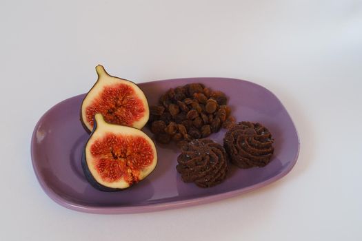 Exotic fruit. Cut figs, raisins and chocolate delicacies on a beautiful plate. Close-up, white background.