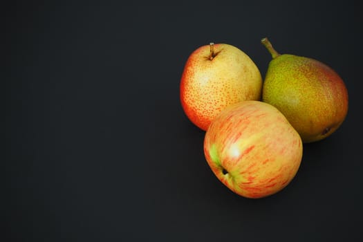 Beautiful pears and an apple on a black background. Ripe fruit. Horizontal image.