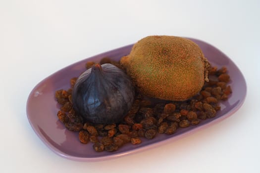 Exotic fruit. Purple figs, kiwi and raisins on an oval dish. Close-up, white background.