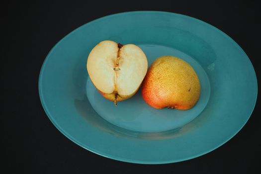 Ripe fruit. Pear on a platter cut into pieces. Black background, horizontal image.