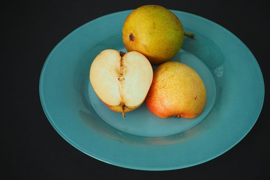 Ripe fruit. Pear on a platter cut into pieces. Black background, horizontal image.