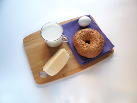 A piece of cheese with baguette and a glass of milk on a wooden tray.