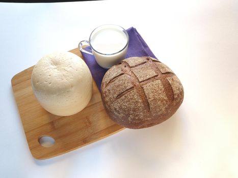 The cheese is a round head cut with bread, baguette, sesame bun. glass of milk on a wooden tray, a piece of cheese. 