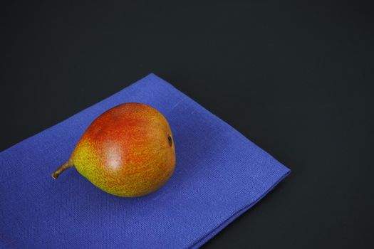 The ripe pear lies on a blue linen napkin. Color photo. Black background. Bright image.