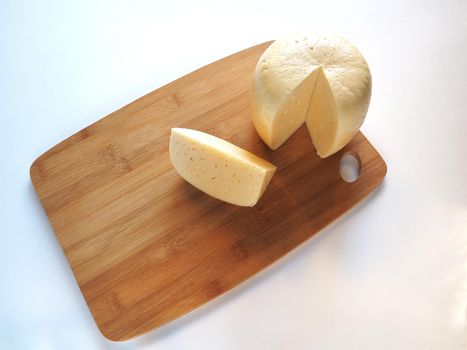  A piece of milk cheese on a wooden board is close-up.