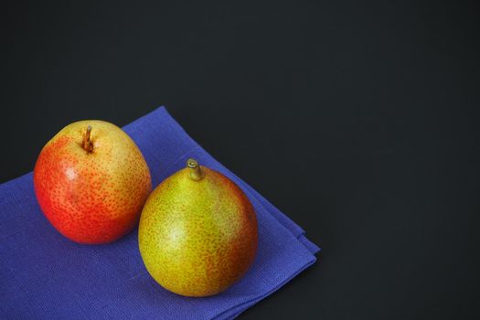 Two ripe pears on a blue napkin, a close-up, a black background. Bottom left.