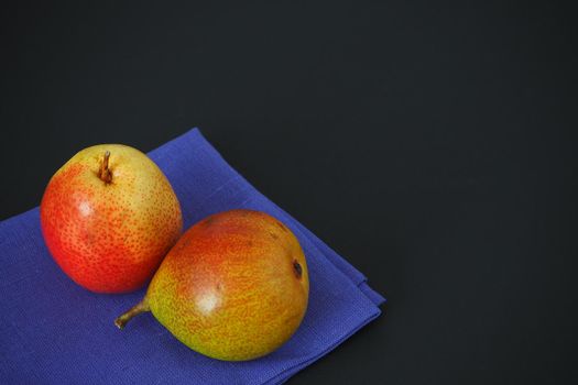 Ripe fruit. Two beautiful pears on a blue cloth napkin. Black background. Horizontal image.