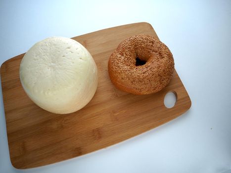 Round head of cheese with a sesame bun on a wooden tray close-up, view from above, white background.