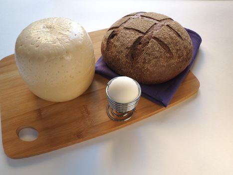 The cheese is a round head cut with bread, baguette, sesame bun. glass of milk on a wooden tray, a piece of cheese. 
