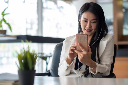 Relax Time - Businesswoman with headphones using smartphone for listening music sitting at the desk indoors in office