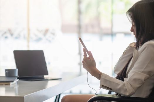 Relax Time - Businesswoman with headphones using smartphone for listening music sitting at the desk indoors in office.