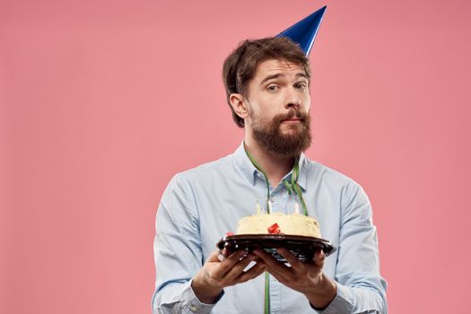 Man with cake in a plate and in a blue shirt on a pink background birthday holidays cropped view. High quality photo