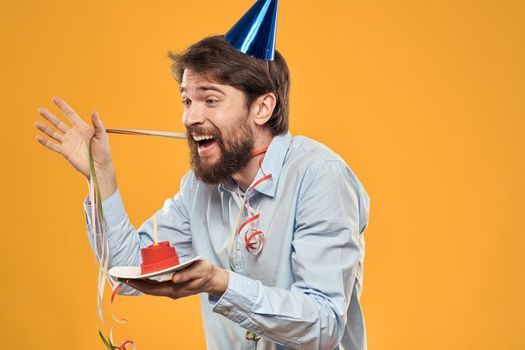 Cheerful man with a cake on a yellow background birthday holidays cap on his head. High quality photo