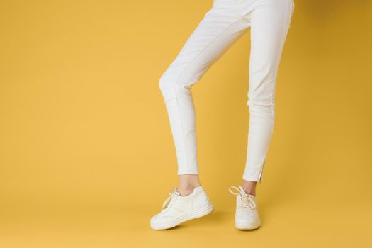 Womens legs white pants sneakers fashion clothes luxury street style yellow background. High quality photo