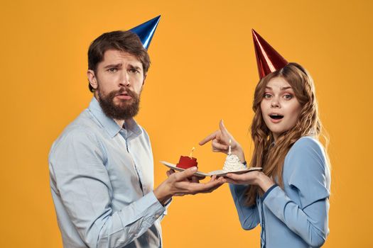 Birthday party man and woman in a cap with a cake on a yellow background cropped view. High quality photo