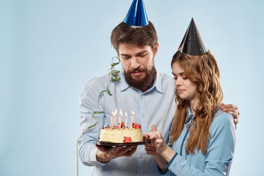 Birthday man woman in party hats on a blue background and cake with candles. High quality photo