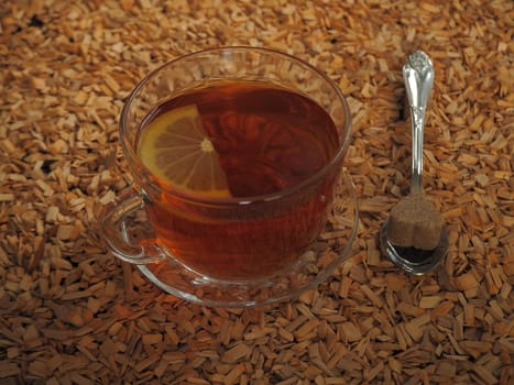 Black tea with lemon in a transparent cup on a wooden tray.