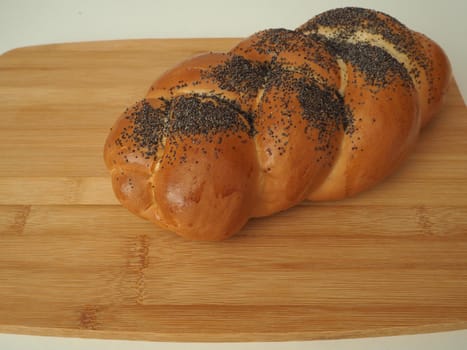 Fresh bread on a wooden tray. A cosy bun with a close-up poppy. White background.