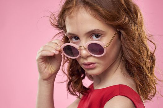 Girl with curly hair dark round glasses fun red dress pink background. High quality photo