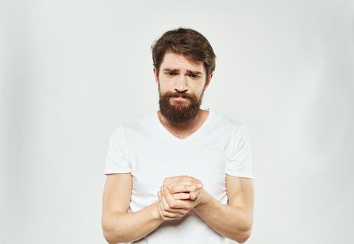 Puzzled man in white t-shirt gesturing with hands cropped view light background. High quality photo