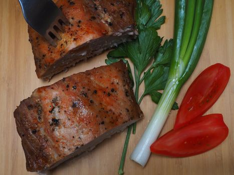 Baked meat on a platter with tomato and herbs. Pork carbonate.