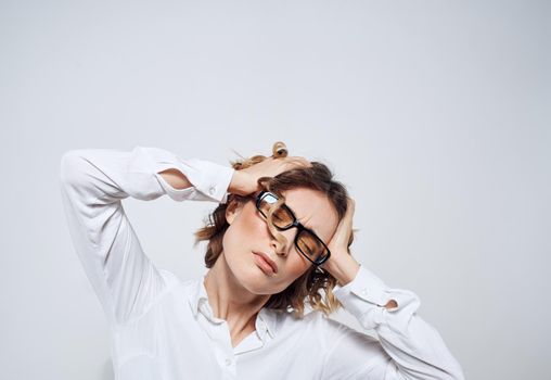 A woman with glasses and a white shirt touches her head with her hands. High quality photo