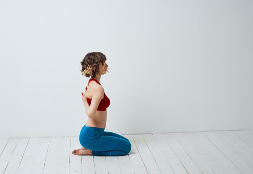 A woman in blue leggings sits on a light floor indoors and holds her hands behind her back. High quality photo