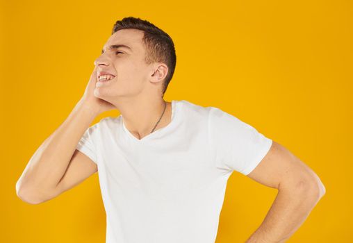 A man in a white T-shirt touches his face with his hand on a yellow background of emotion. High quality photo