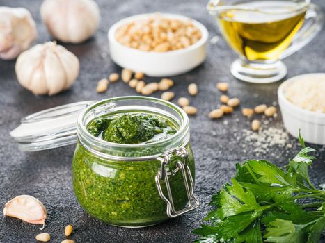 Homemade parsley pesto sauce and ingredients on dark cement background. Close up wiev of parsley pesto in glass jar with ingredients.