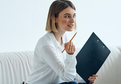 A woman sits on a sofa In a bright room in a shirt and papers . High quality photo