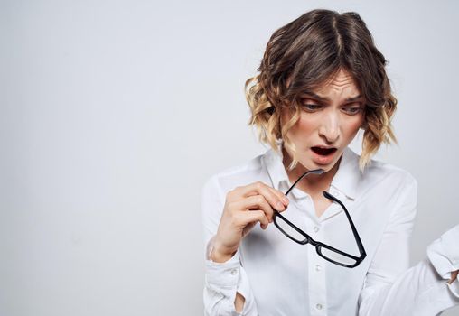 A beautiful woman in a white shirt holds glasses in her hands on a light background. High quality photo