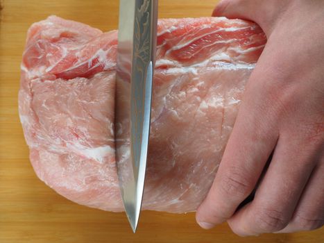 Fresh meat. A man cuts meat into pieces on a wooden board.