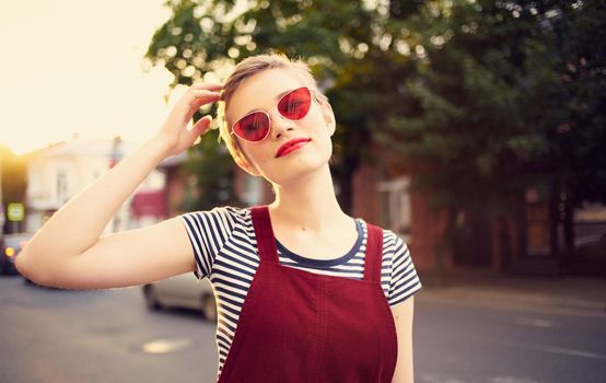 romantic woman in a sundress and red glasses walks along the city street in summer. High quality photo