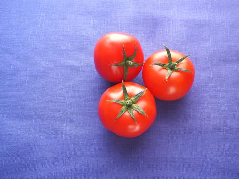 Food. Vegetables. Three tomatoes are red, close-up, on a blue background.