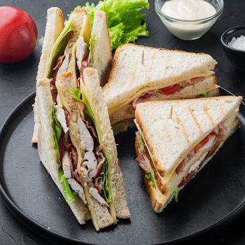 Club sandwich with meat, cheese tomato, ham, on black background
