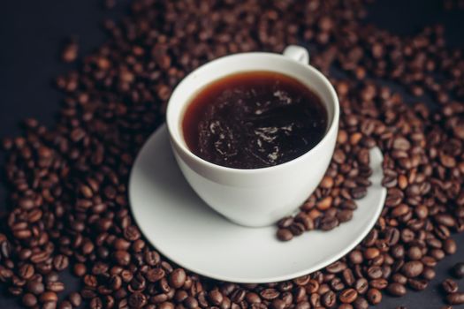 coffee beans and a cup on a white saucer dark background drink. High quality photo