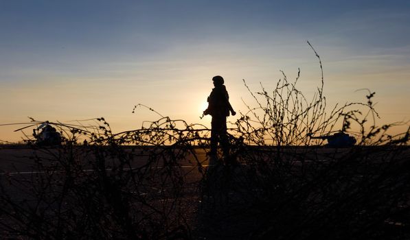 MARIUPOL, UKRAINE - Nov. 16, 2017: Silhouette of a military man with a machine gun in a combat post against the helicopters and sunset sky during festivities on occasion of the Day of Naval Infantry