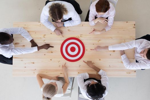 Team of business people pointing at red goal target at meeting table aiming strategic marketing on dartboard bullseye targeted creative idea achievement strategy development concept