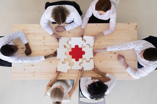 Group of business people assembling jigsaw puzzle sitting around table, team support and help concept