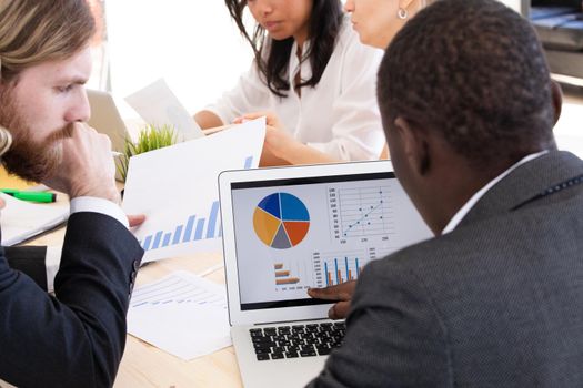 Diverse executive business people team discussing work results at meeting, multiracial businessmen talking analyzing financial statistics report sitting together in modern office