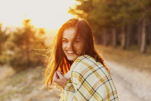 woman with a blanket on her shoulders laughs the sunset in the background and conifers on the side. High quality photo
