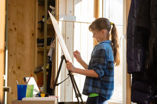 A ten-year-old girl makes a sketch on an easel, removes unnecessary details with a washing eraser