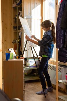 A ten-year-old girl draws with paints on an easel at home