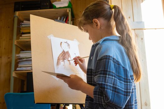 A ten-year-old girl draws with paints on an easel