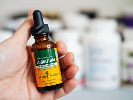 Moscow, Russia - March 09, 2021: Glass bottle with Lomatium in female hand and others nutrition supplements in blurred background. Lomatium liquid extract by Herb Pharm for Immune Support