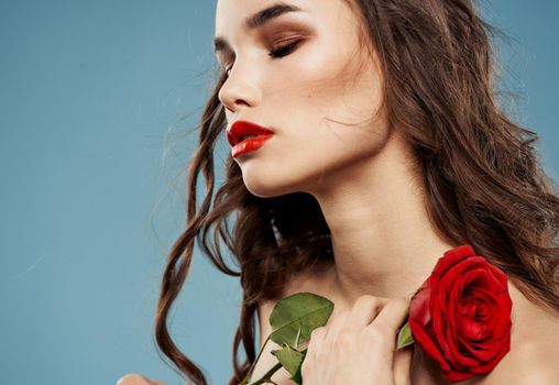 Sexy woman with red rose and blue background with brunette curls. High quality photo